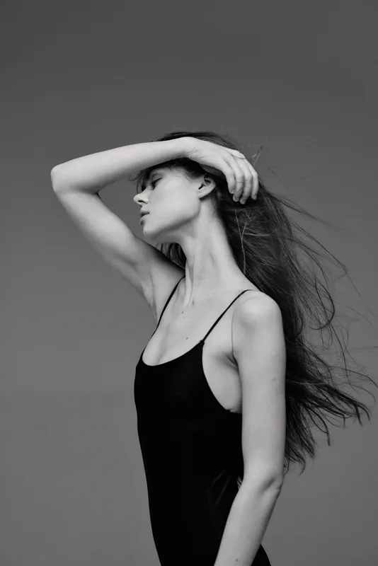 Black and white profile of a slender woman with flowing hair in a sleeveless top, expressing calm and elegance against a plain background.
