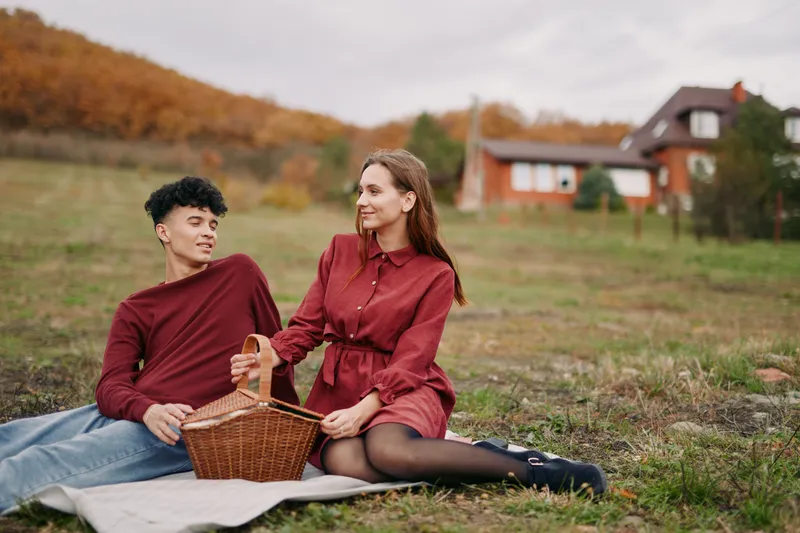 A candid outdoor picnic scene with a couple on a blanket, a wicker basket nearby, autumn field and soft light creating an authentic, natural mood.