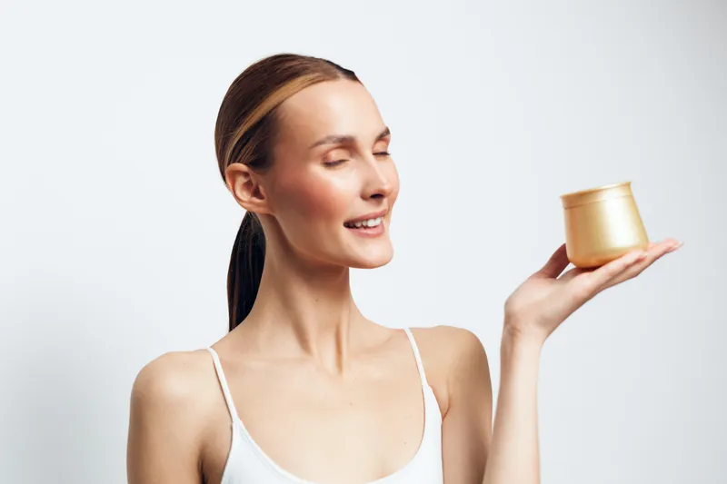 Woman holds scented candle in studio portrait, spa relaxation concept, aromatherapy aroma ritual, serene expression with eyes closed, soft light on white background, minimal calm mood