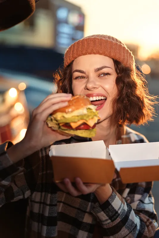 woman smiling with burger outdoor at golden hour, candid authenticity in a warm urban portrait holding takeout box. Emotional storytelling, mindful living and golden glow capture sincere joy.