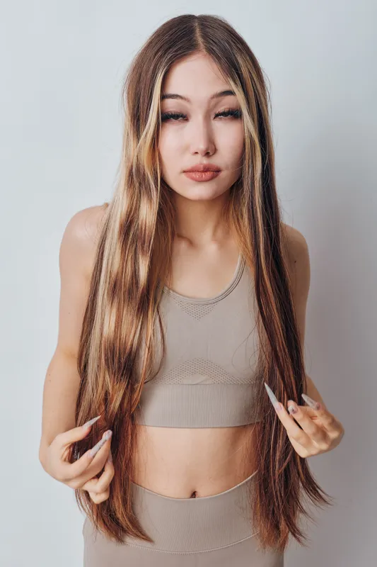 Young woman with long straight hair in beige sportswear posing indoors on light background. Beauty, fashion and casual style for lifestyle and health concept.