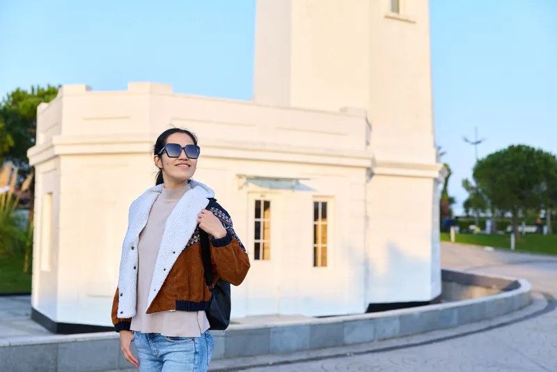 Fashion, woman, sunglasses, jacket, bag, monument, outdoors, sunlight capture a stylish model posing near a historic structure on a sunny day, showcasing confident streetwear chic layering, urban