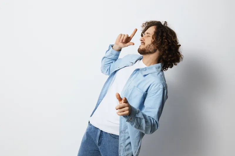 Happy young man expressing joy with playful gestures, wearing casual clothing, against a light background, ideal for concepts like celebration or positivity