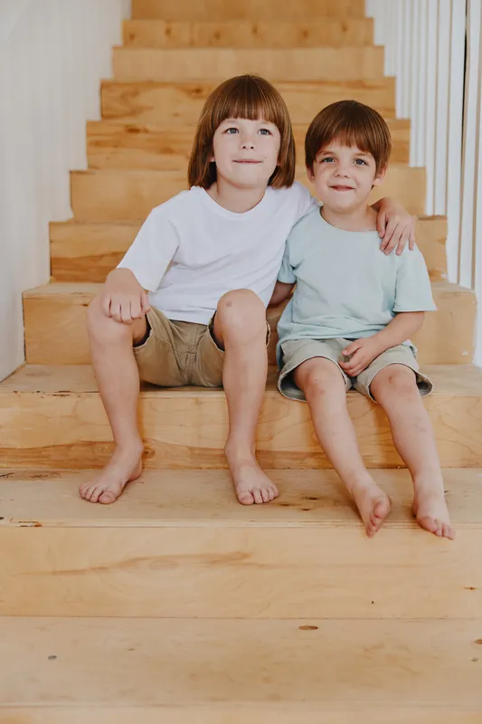 Two smiling boys sit on wooden stairs, showcasing a cheerful moment of friendship and playfulness with natural, warm lighting.