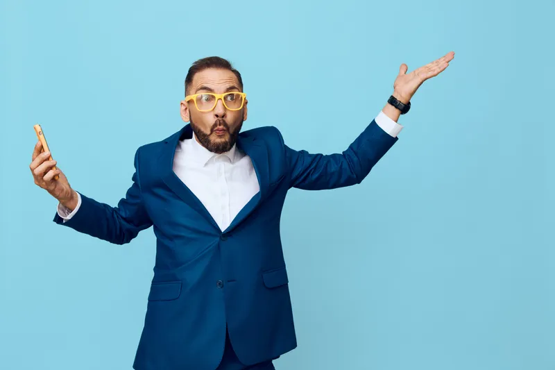 Businessman in a blue suit on a solid blue background, displaying confident yet playful emotion. Isolated color backdrop highlights professional style and strong character for corporate stock use.