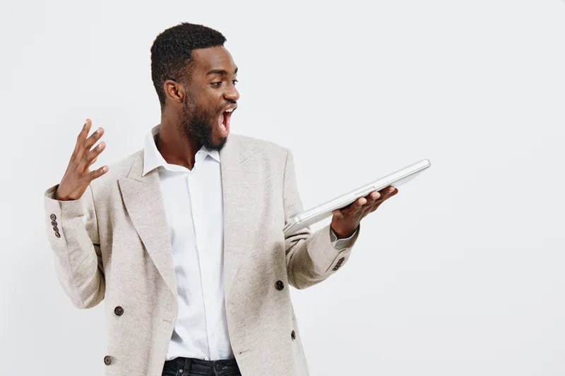 Smiling man holding a tablet with an excited expression, wearing a beige blazer and white shirt, isolated on a plain white background. Business and technology concept, emotions, communication.