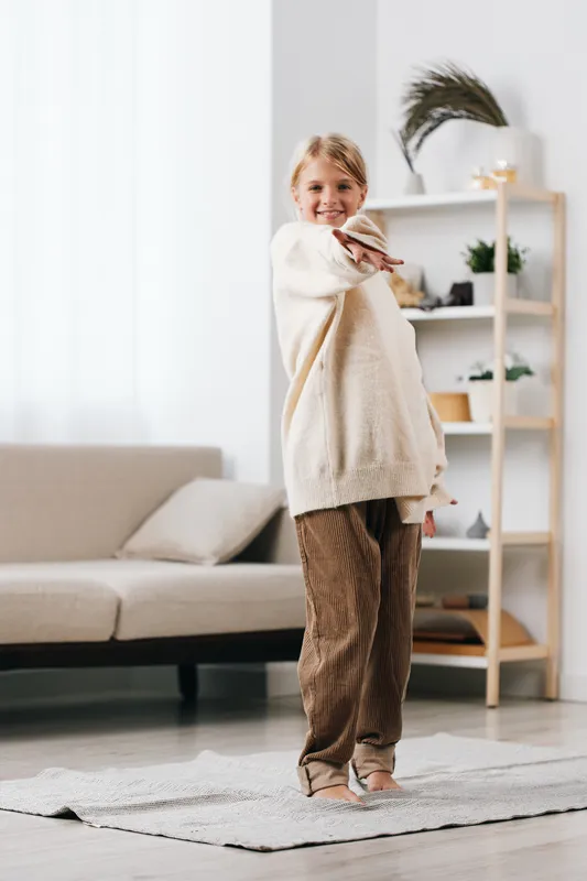 Authentic lifestyle scene features a young child in cozy homewear, moving playfully in a bright living room, capturing genuine everyday life and comfort.