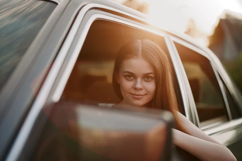 Young girl with long hair smiling from a car window, enjoying a sunset drive, evoking feelings of freedom and adventure.
