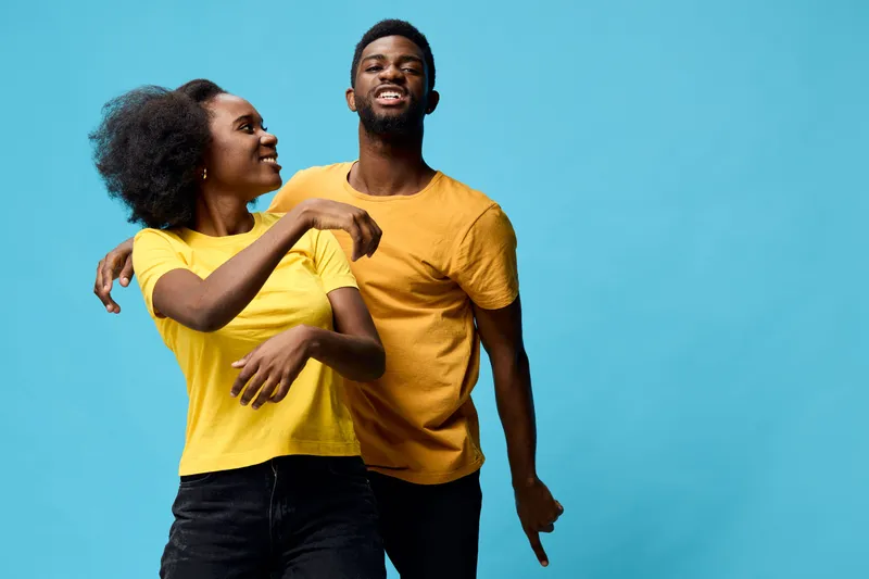 Happy young African American couple in matching yellow shirts against a bright blue background, showcasing joy and connection in a vibrant, playful atmosphere