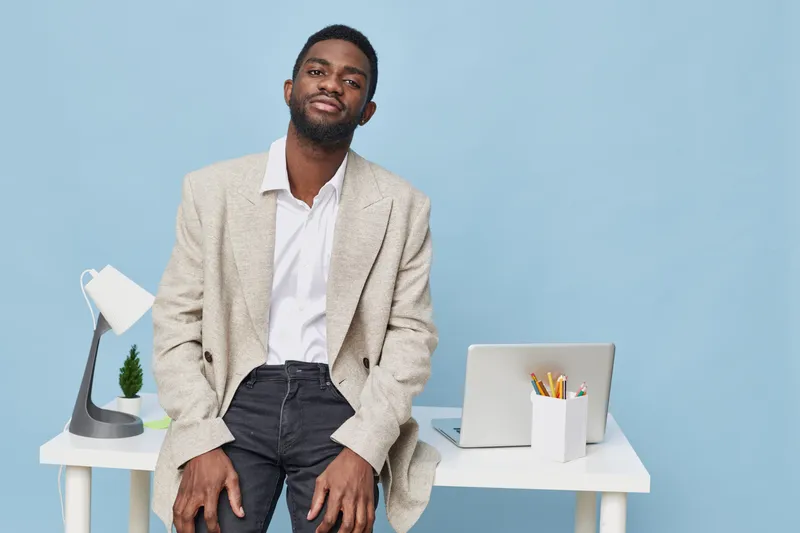 Confident man in casual blazer and white shirt sitting at modern desk on blue background workspace lifestyle concept
