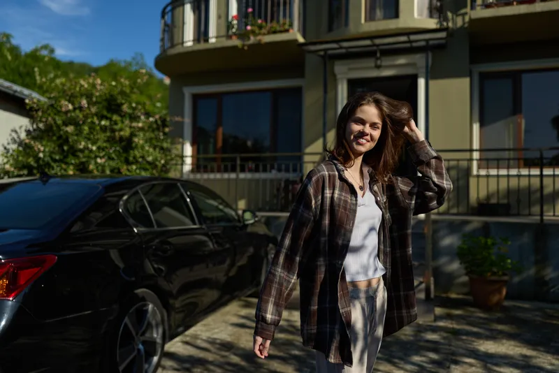 Casual woman outdoors in sunlight, wearing a plaid shirt and light jacket, walking on a sunny street with a relaxed smile and natural breeze
