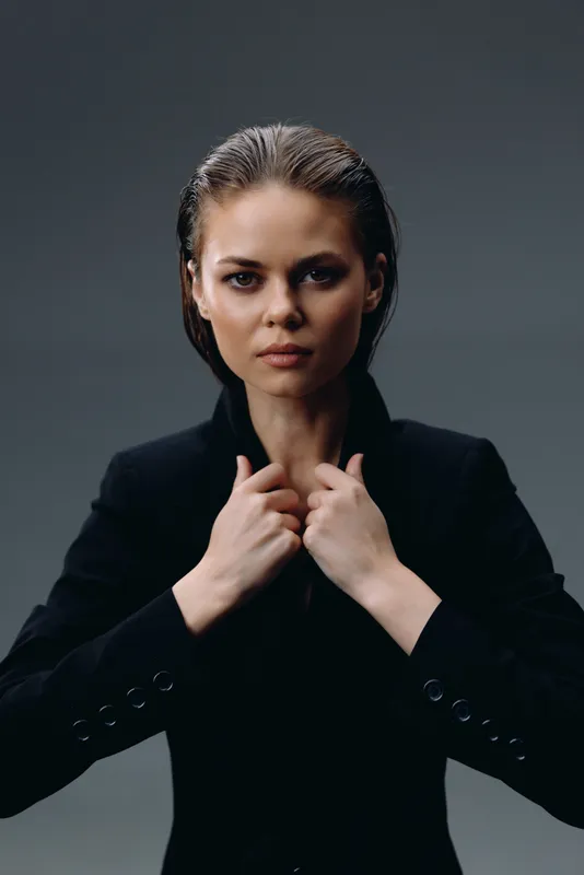 confident woman in black jacket with intense expression in dark studio setting