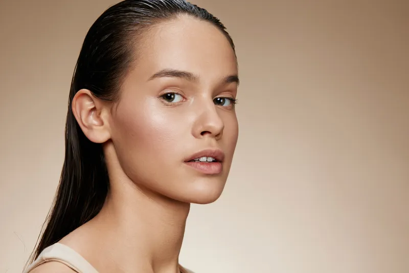 Young woman with natural beauty and minimal makeup on a neutral background, showcasing healthy skin and subtle elegance