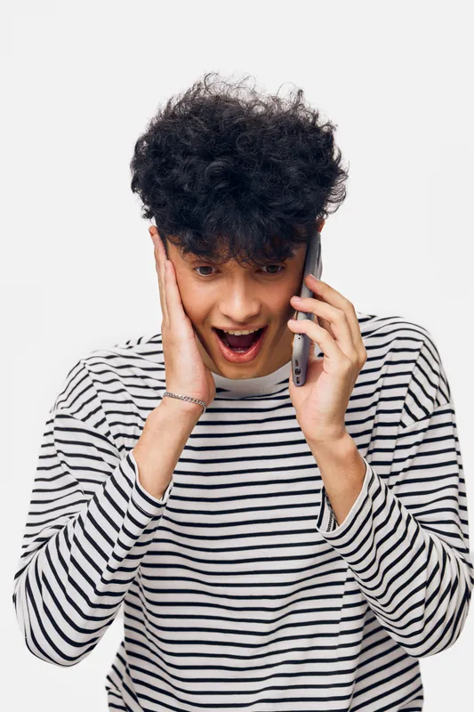 surprised man talking on phone wearing striped shirt expressing shock and excitement with curly hair, isolated on white background