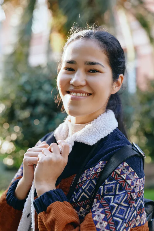 Smile, woman outdoors in a patterned cardigan and warm jacket, casual fashion in a sunny park, candid lifestyle moment highlighting comfort and style