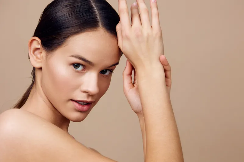 Beautiful young woman showcasing flawless skin with a soft expression, emphasizing natural beauty against a neutral beige background perfect for health and wellness themes