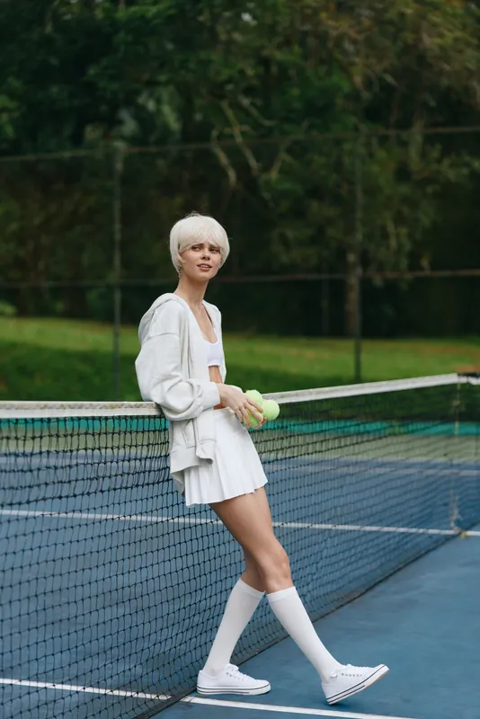 Young woman with short white hair in sporty attire stands confidently on a tennis court, exuding a healthy lifestyle and athletic spirit