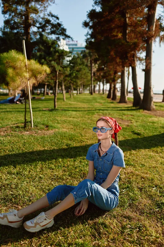 lifestyle woman in modern boho-western denim street style sitting relaxed outdoors wearing sunglasses and a red bandana with vibrant film color tones