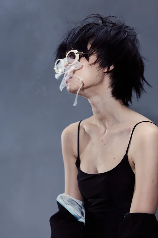 young woman blowing smoke rings wearing black top with casual hairstyle