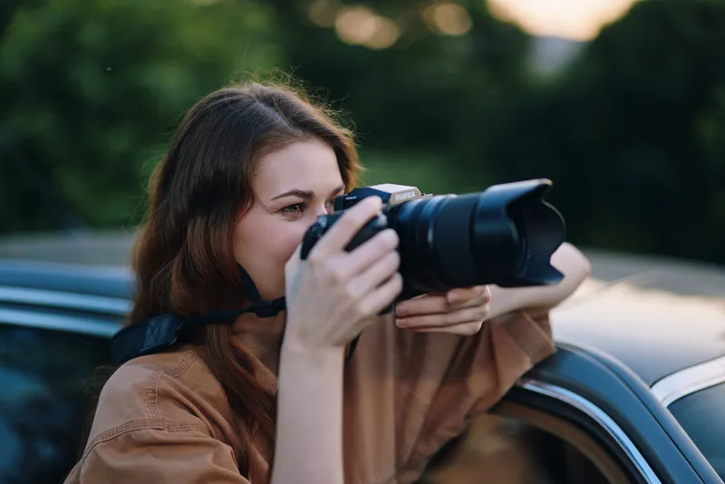 Young woman capturing nature with a camera in a casual setting, showcasing creativity and passion for photography, highlighting emotions and outdoor beauty.