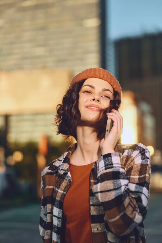 Woman on phone smiling in urban street during golden hour glow, a candid lifestyle portrait capturing authenticity, mindful living and emotional storytelling with warm city atmosphere.