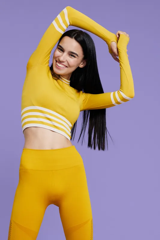 woman sport fitness stretching in yellow activewear smiling confidently against purple background, healthy lifestyle, wellness, energy, flexibility, joy