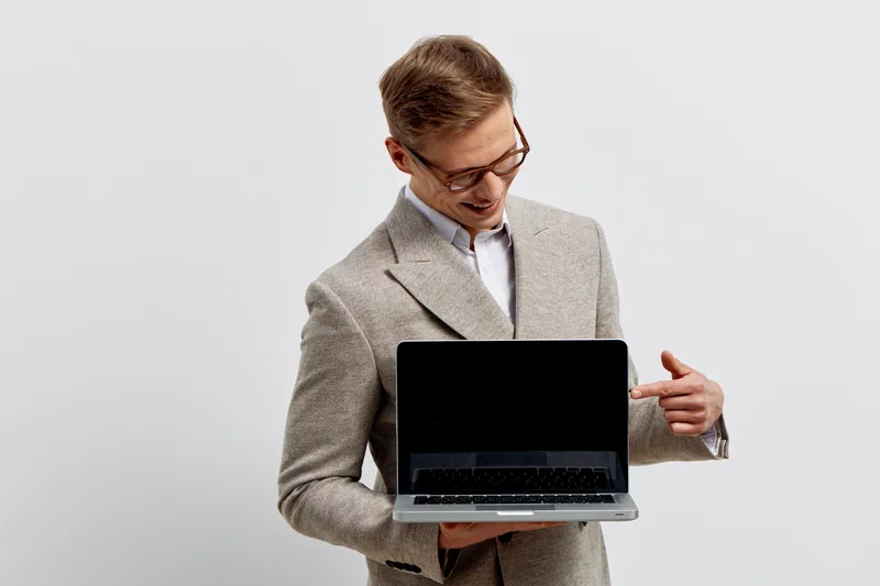 young smiling caucasian man wearing gray suit glasses hold show laptop blank screen digital nomad work remote technology concept isolated light background