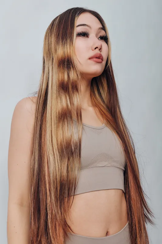 Young woman with long straight hair and natural makeup posing in beige top against light background with serious expression and confident posture indoors.