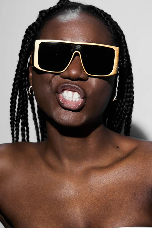 Confident Black woman with braided hair wearing oversized sunglasses and a bold expression against a minimalist background, showcasing modern fashion and attitude