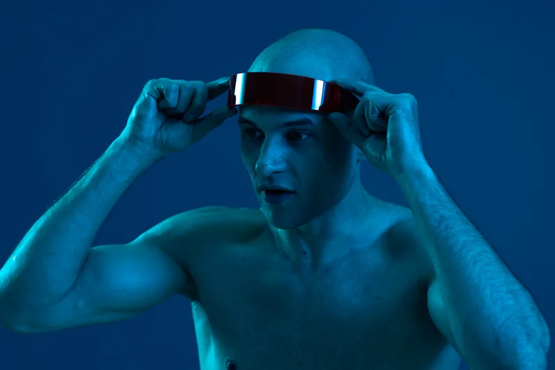 A focused man adjusts a futuristic headband, showcasing determination and innovation in a captivating blue light setting. Perfect for technology and wellness themes.