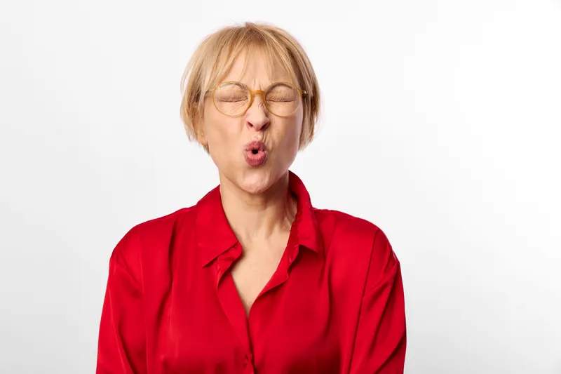 Blonde woman with glasses wearing red shirt singing with eyes closed, mouth open, expressive studio portrait on white background, calm sincere mood, copy space