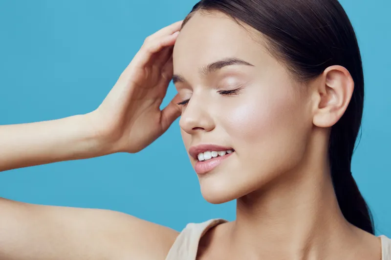 Young woman with smooth skin and serene expression, showcasing beauty and confidence against a bright blue background Season summer