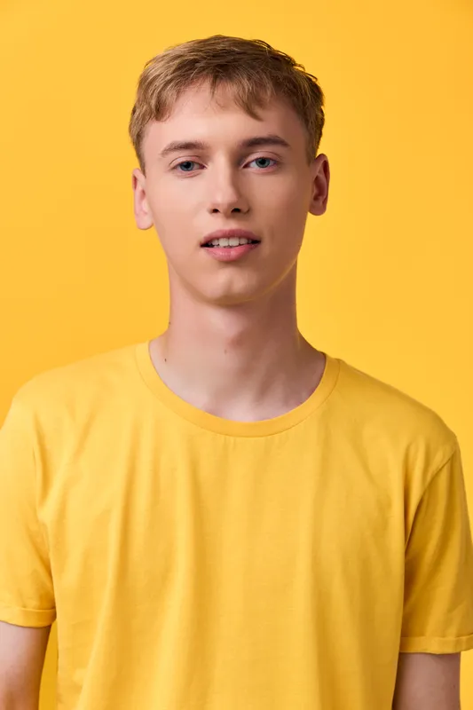 Young man in a yellow tee stands against a bright yellow backdrop, casual style and relaxed expression, clean studio shot for lifestyle and fashion campaigns.