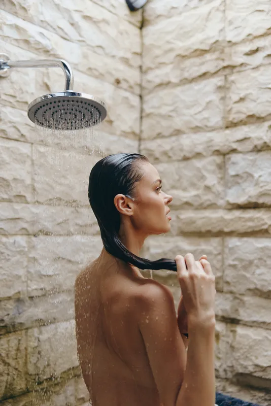 naked woman taking shower in rustic stone bathroom, wet hair, side profile, refreshing morning routine, natural light, wellness moment