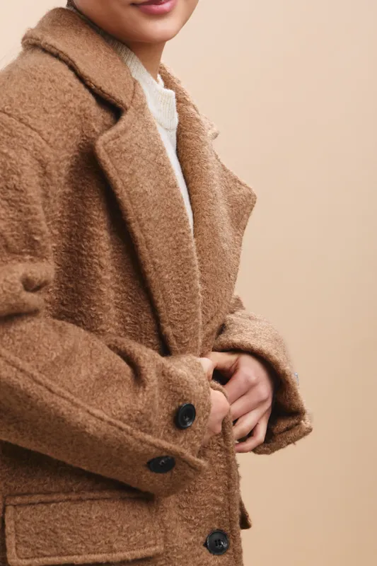 asian woman wearing a warm brown coat stands against a neutral backdrop, presenting a stylish pose with graceful posture and calm confidence, inviting a refined fashion and lifestyle vibe.