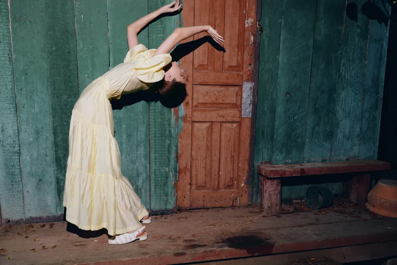 dancer in a yellow dress bends into a graceful pose near a doorway in a vintage worn interior showcasing movement posture and arched lines
