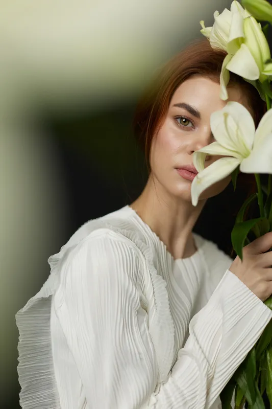 Elegant woman holding white lilies in soft, dreamy background, showcasing beauty and serenity, perfect for health and wellness themes