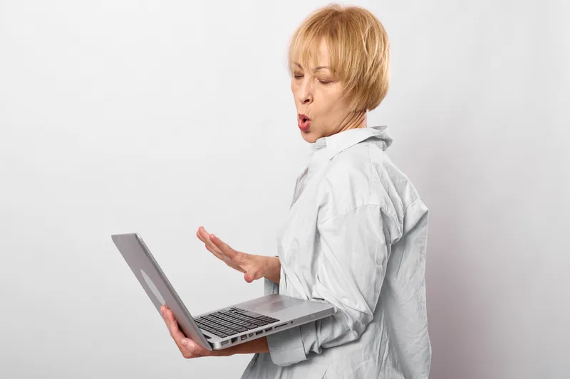 Woman healthcare worker in white coat, surprised expression, speaking with laptop, remote online communication, stress and workload concept clinic care