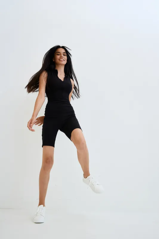 active woman jumping in black athletic outfit and white sneakers against clean bright background, energetic motion, fitness and healthy lifestyle concept.