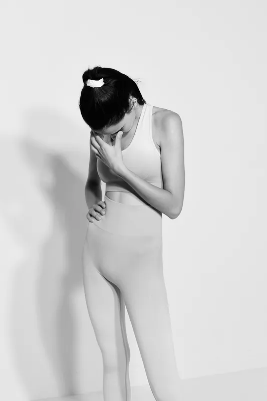 Young woman sport fitness dressed in seamless activewear stands with thoughtful pose against white background in black and white photography, reflecting calm and focus.