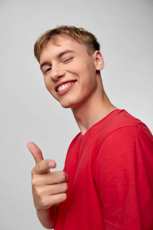Smiling man in a red shirt points playfully at the camera, radiating confidence, friendliness, and a bright studio mood, ideal for lifestyle, marketing, and upbeat messaging.