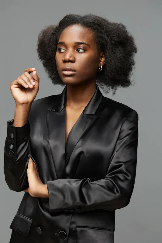Elegant African woman in a black satin blazer, exuding confidence with a thoughtful expression against a neutral grey background