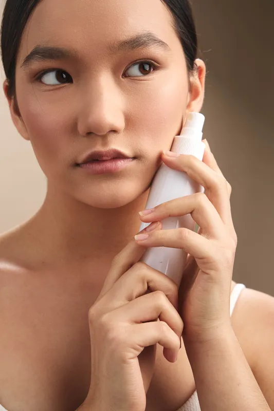 Asian woman is pictured in a closeup, holding a phone to her ear in a calm, intimate moment. Her serene expression and soft lighting convey focus and quiet confidence.