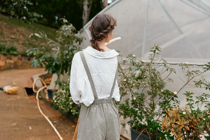 Young woman in casual clothing walking in a garden, surrounded by plants in a greenhouse, showcasing a peaceful connection with nature and sustainable living