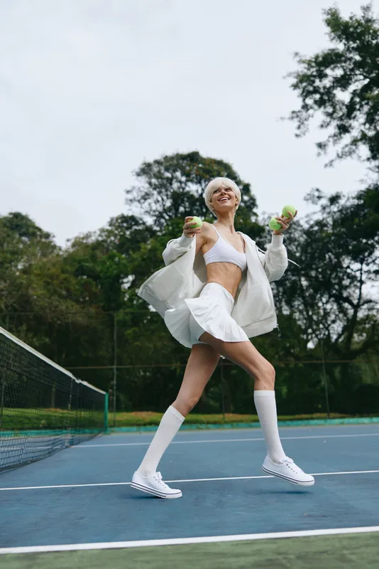 Energetic young woman in sporty attire joyfully playing tennis outdoors, showcasing athleticism and style on a green tennis court