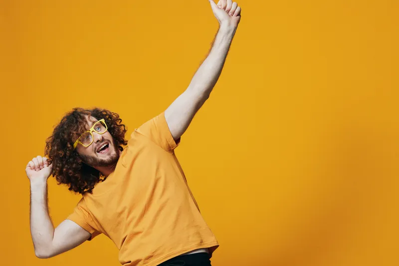 Cheerful young man in a yellow t shirt and glasses celebrating against a bright yellow background, conveying joy and positivity in lifestyle imagery