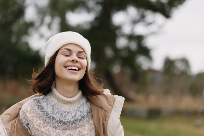 Woman, smile, outdoors, winter, cozy, casual portrait in natural light wearing a knitted sweater, beanie and warm jacket enjoying fresh air and a carefree moment