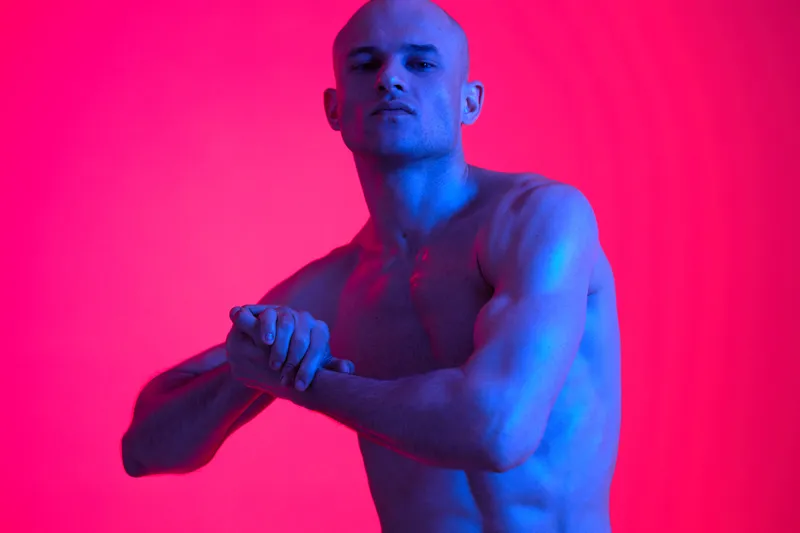 A confident man poses dramatically against a vibrant, abstract background, showcasing bold colors and striking lighting. The image captures intensity and emotion.
