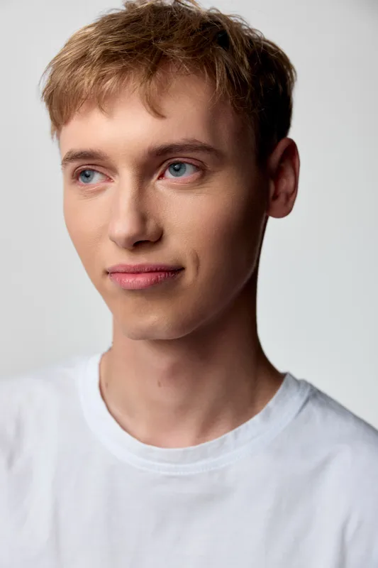 Young man with calm expression in a studio shot, wearing a casual white shirt, closeup framing, soft lighting and clean minimalist mood for lifestyle or fashion projects