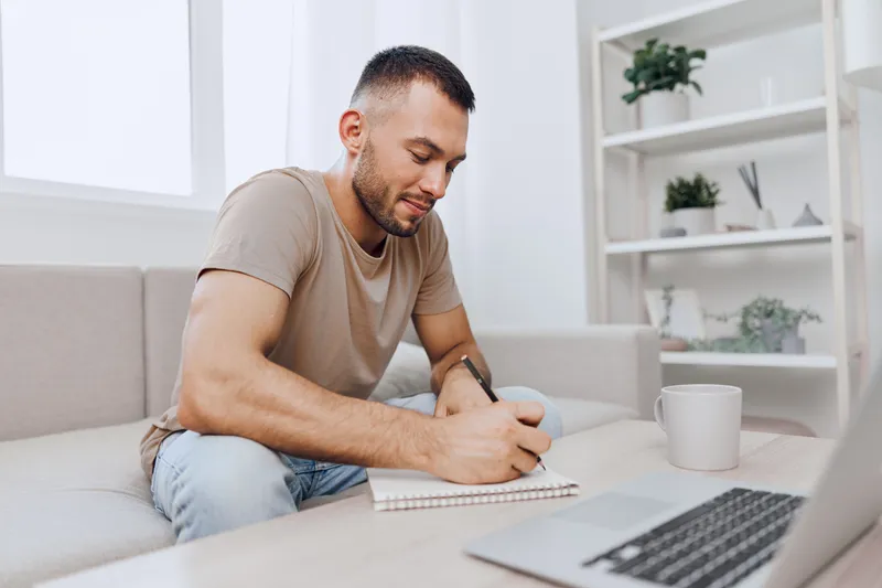Thoughtful man sketching ideas in a notebook at home, surrounded by plants, cozy atmosphere, modern decor, focusing on creativity and inspiration.